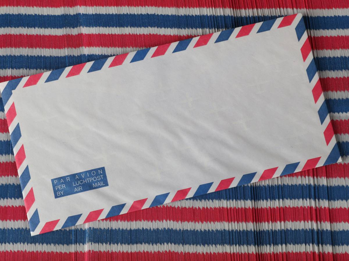 A church administrator in a quiet office organizing a stack of weekly bulletins and applying bulk patriotic stamps to ensure delivery to senior members.